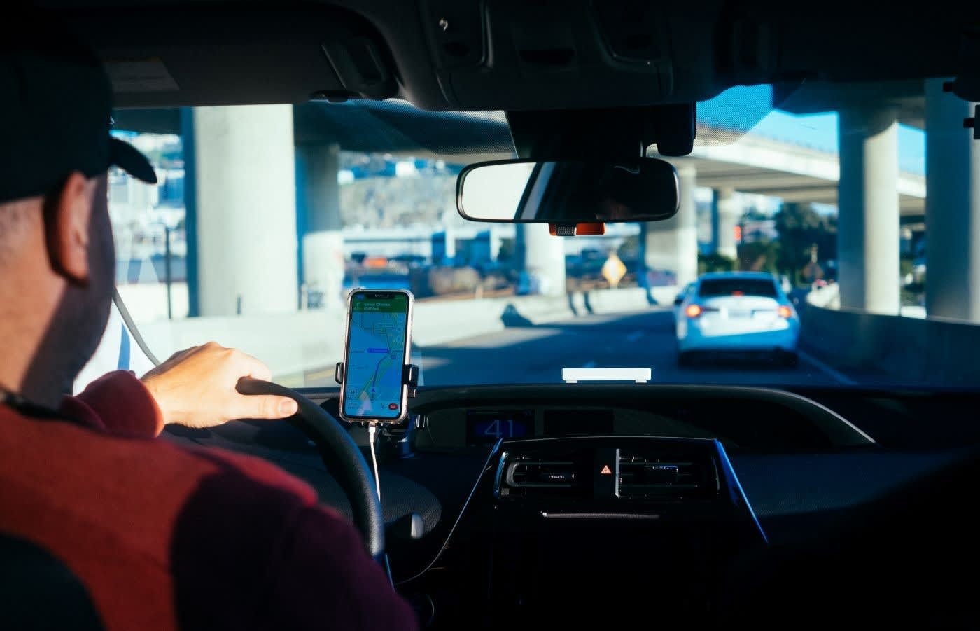 A man using a mobile phone for navigation while driving a car, highlighting the ease of use of car share programs.