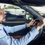 A man is shown pressing the HomeLink buttons located on his car's rearview mirror to program his garage door opener.