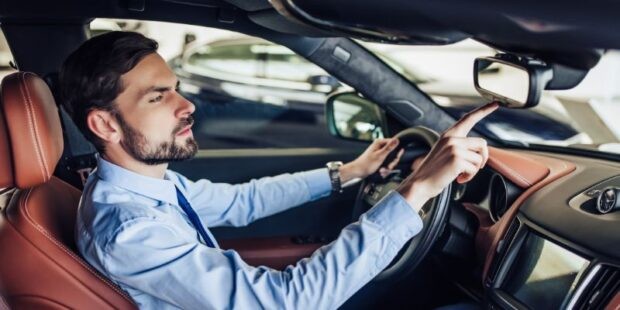 A man is shown pressing the HomeLink buttons located on his car's rearview mirror to program his garage door opener.