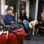 Three individuals and a dog relax on a porch, symbolizing the comfortable and community-oriented atmosphere of the Medical Foster Home program.