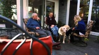 Three individuals and a dog relax on a porch, symbolizing the comfortable and community-oriented atmosphere of the Medical Foster Home program.