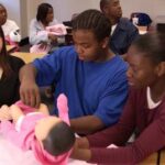 Students interacting with RealCare Baby simulators in a classroom setting, demonstrating hands-on learning about infant care.