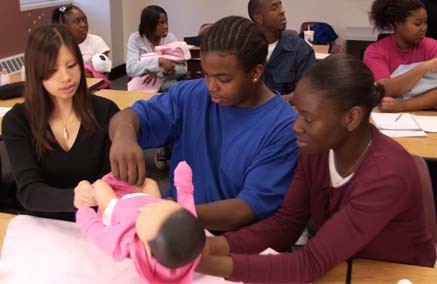 Students interacting with RealCare Baby simulators in a classroom setting, demonstrating hands-on learning about infant care.